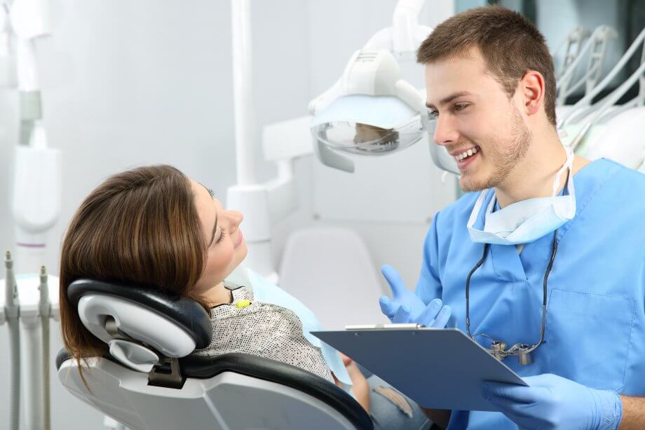 Male dentist smiling and talking to a female patient in a dentist chair.
