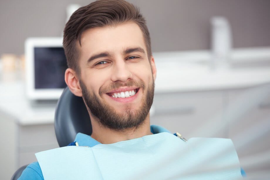 Photograph of a man with short brown hair and a beard smiling while sitting in a dentist chair.