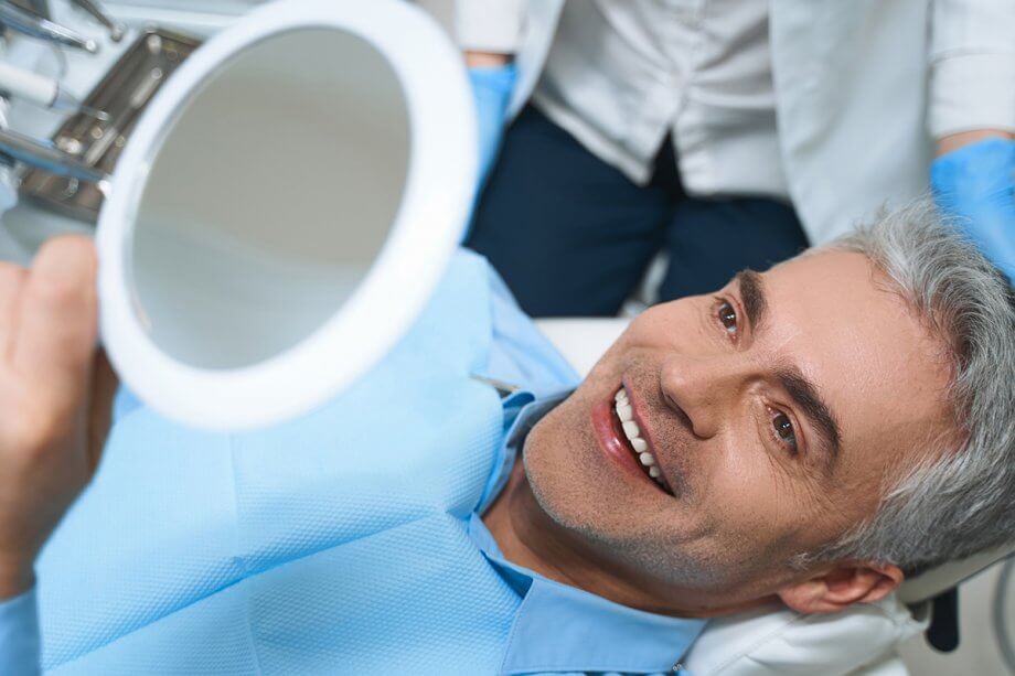 man in dental chair looking at smile in mirror